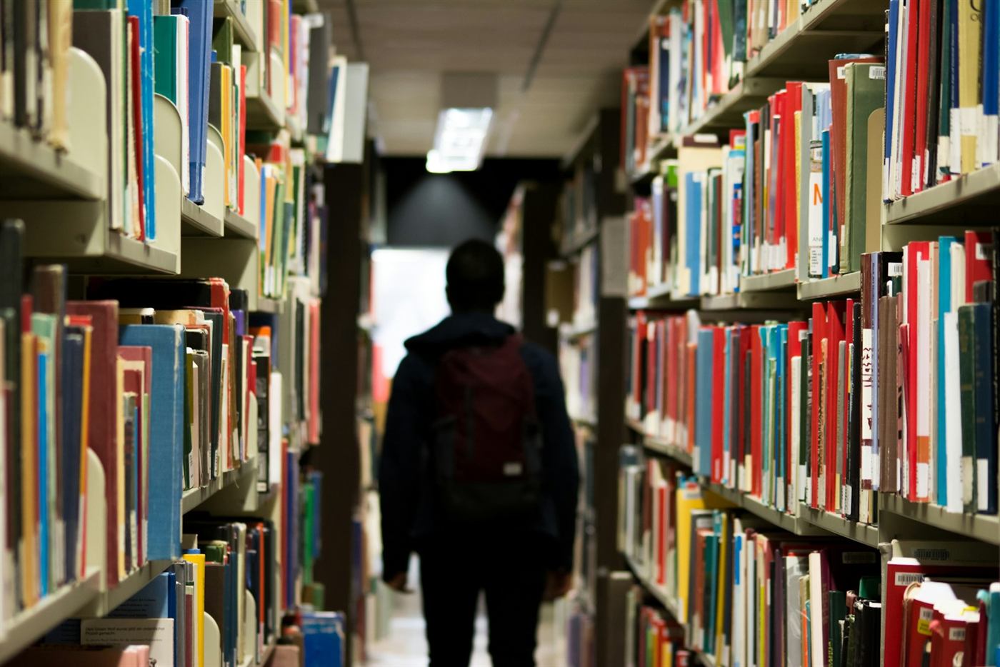 Une personne seule dans une allée de bibliothèque, entre deux murs de livres